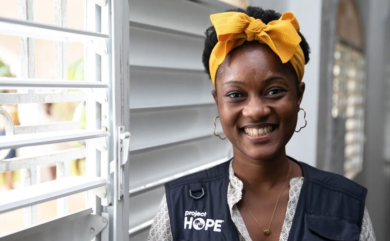 Woman with yellow headband and Project HOPE vest smiles to camera