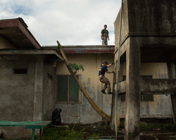 Project HOPE volunteer Paul Holzer, M.D. climbs ladder on Tapaz District Hospital to inspect damage