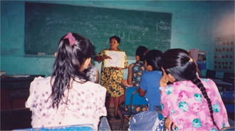 Teacher in front of a classroom pointing to book in hand