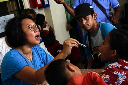 Woman medical volunteers look in throat of girl