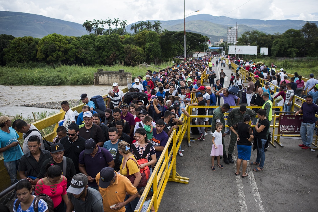 Venezuelans waiting in line behind a yellow fence
