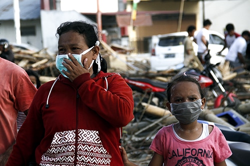Two people with masks on walking over rubble