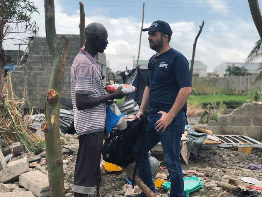 Two men speaking with debris caused by Cyclone Idai in Beira, Mozambique, in the background. 
