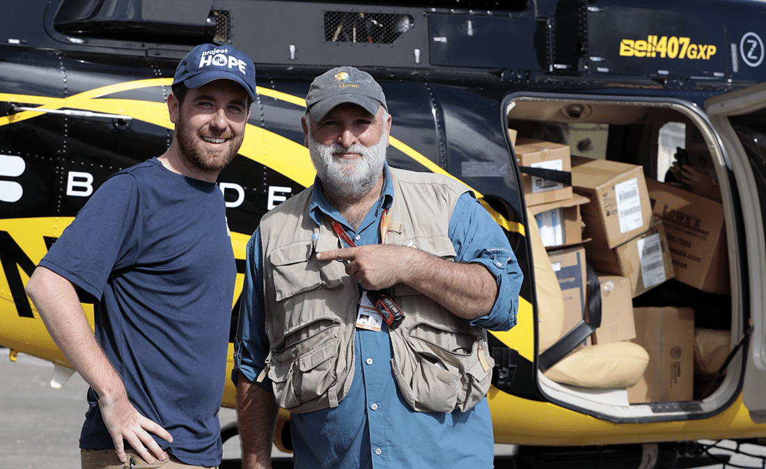 Two men in front of a helicopter filled with boxes