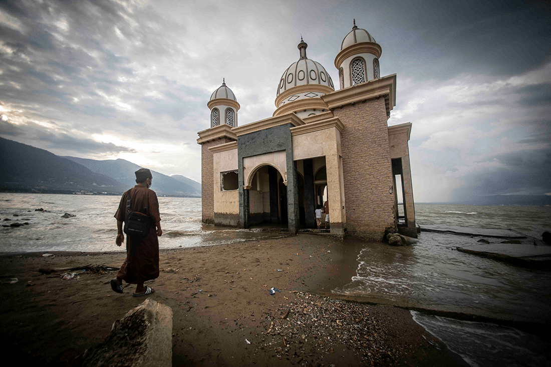 Photo of a man walking towards a mosque that is flooded and sliding into the ocean after an earthquake in Indonesia.
