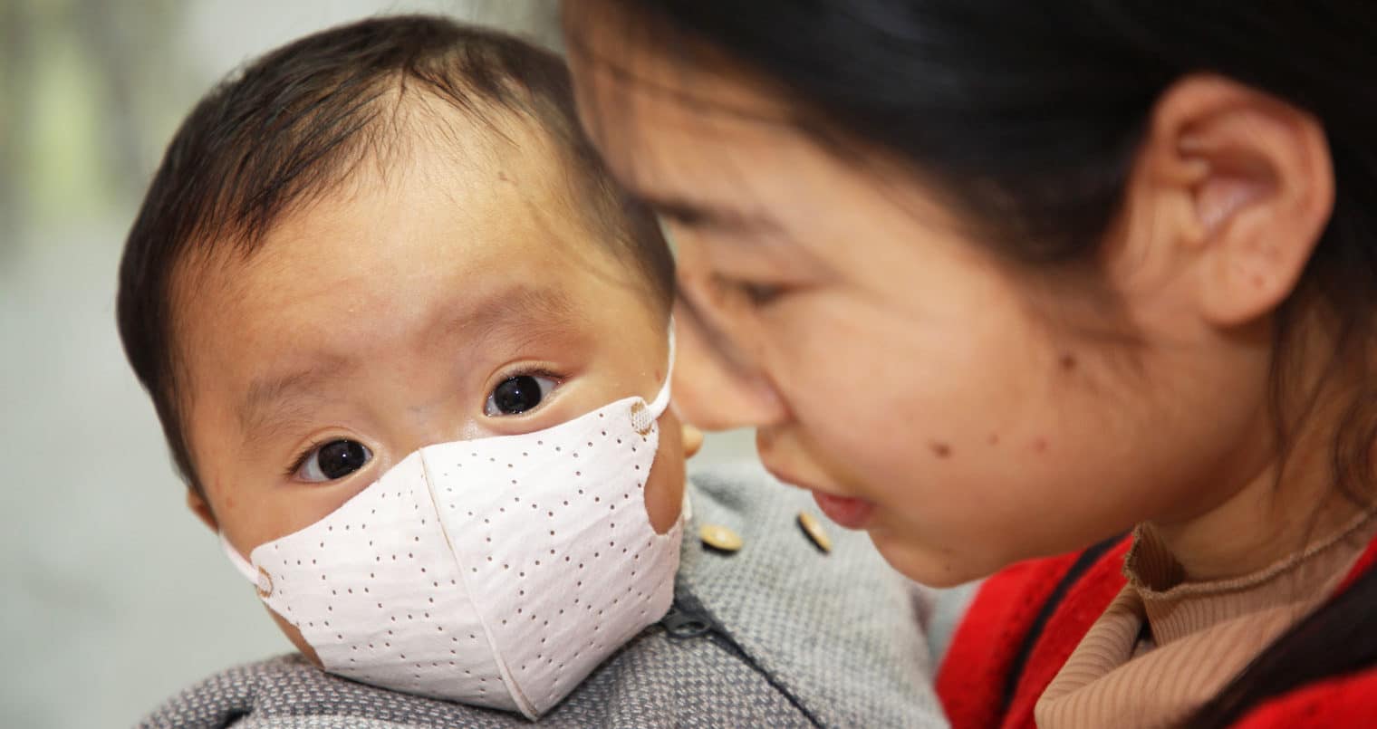 Asian woman holding her child who is wearing a face mask to help prevent catching the coronavirus.
