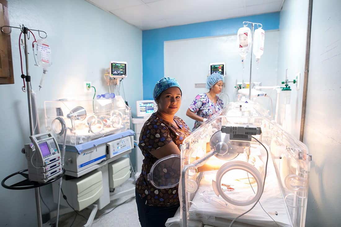 Two nurses working in NICU attending to babies in incubators.