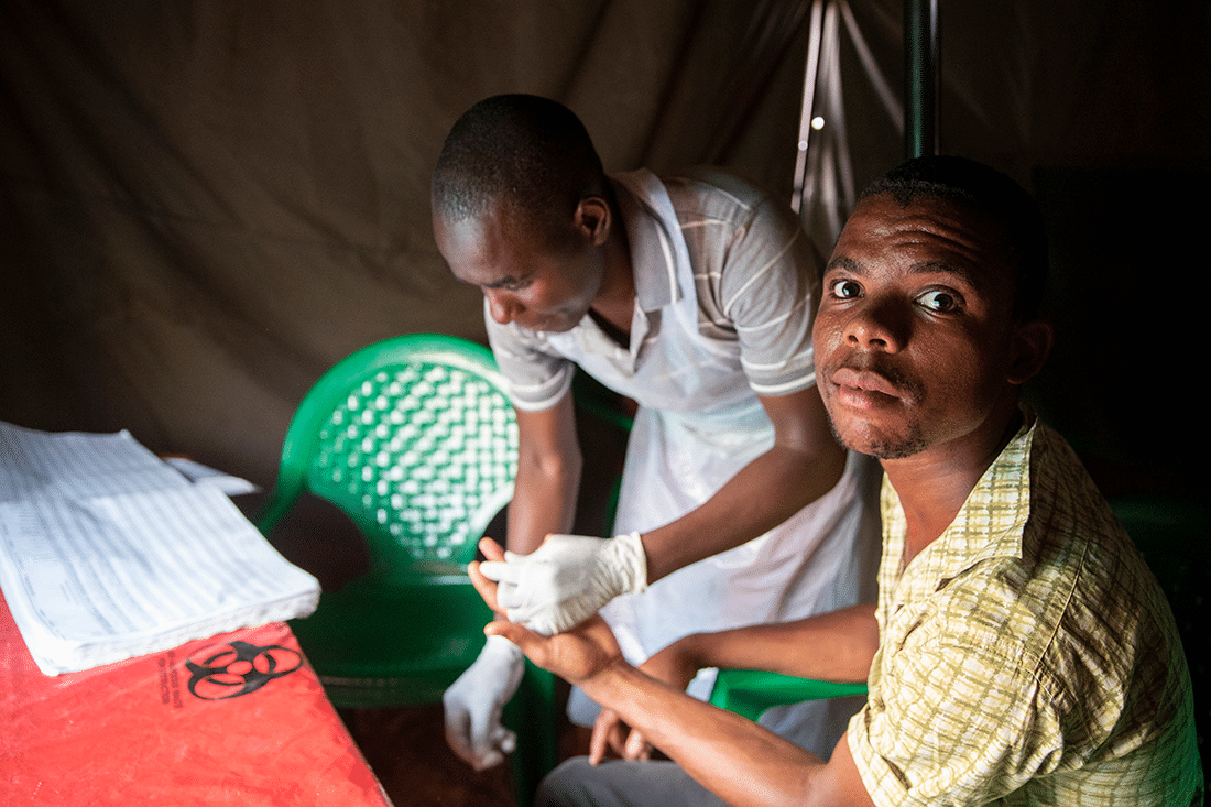 A young man takes an HIV test in a closed tent.