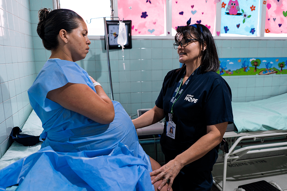 A nurse checks the health of a pregnant patient in a hospital room.