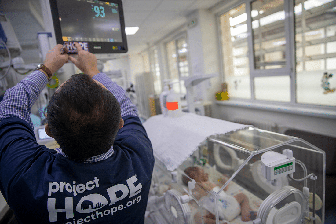 A man adjusts a neonatal monitor in an ICU.