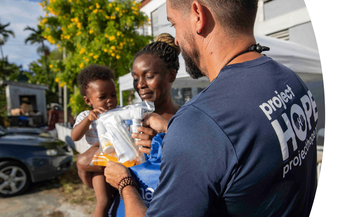 Project HOPE team member distributing supplies to a mother and child