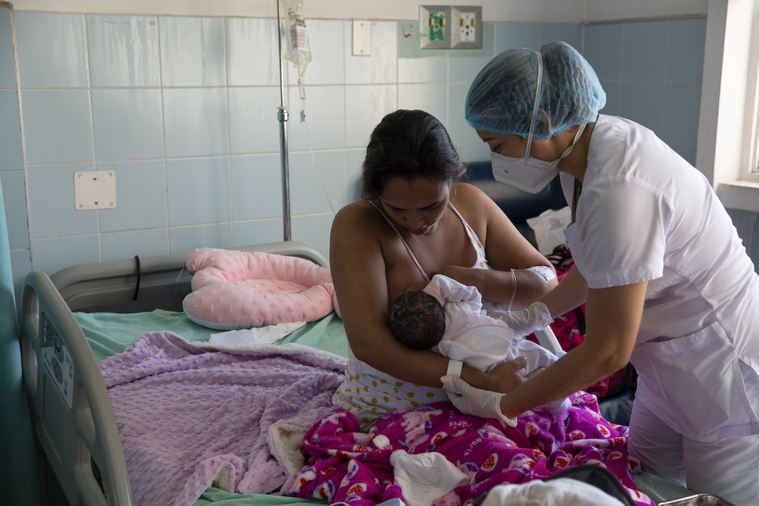 a new mother learning to nurse their newborn baby with the help of a nurse. 