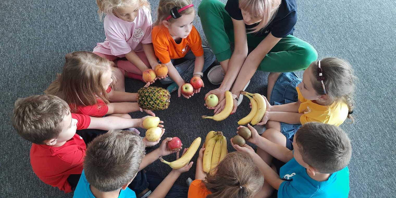 circle of children sitting down holding fruit.