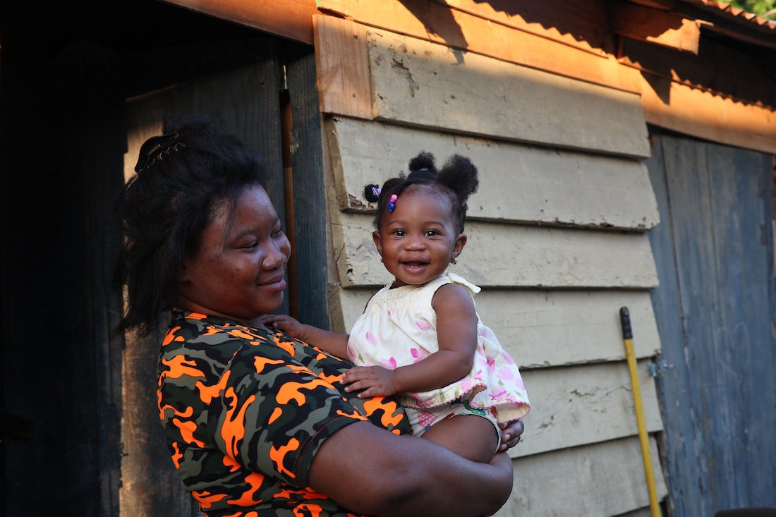 a mother holding a smiling child outside of a house.