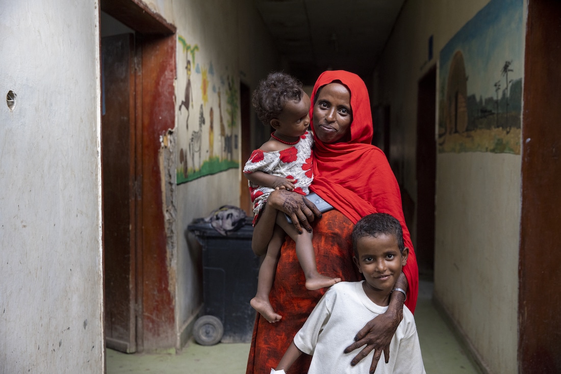 a mother with two children smiling at the camera while standing in a hallway.