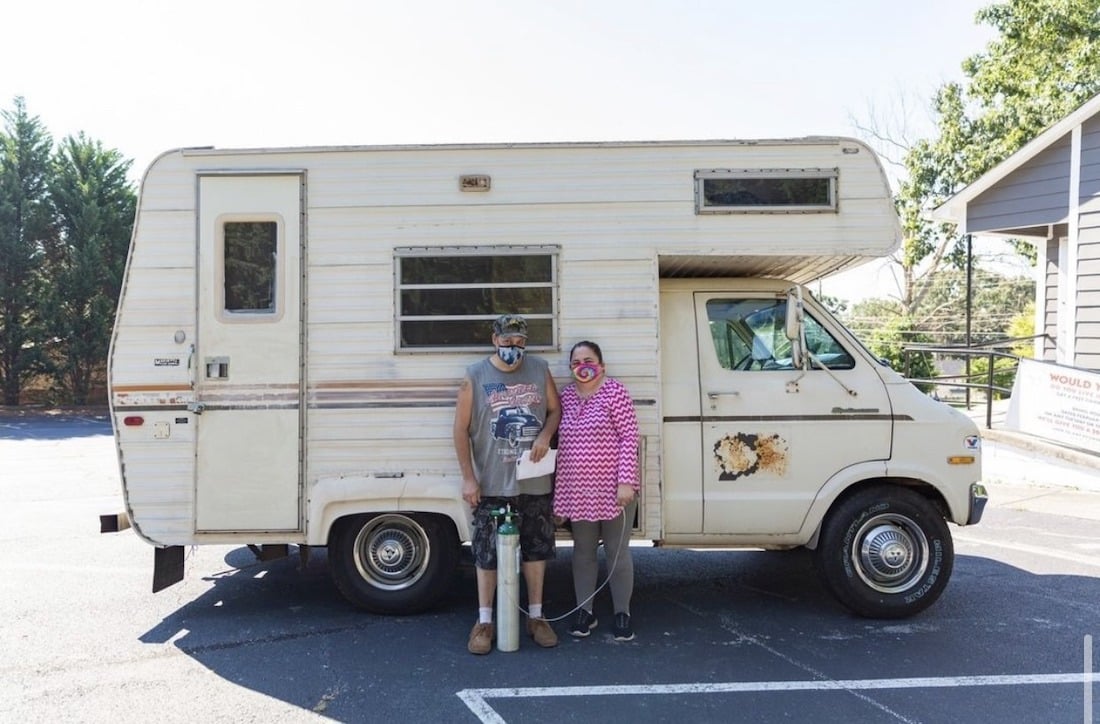 Two people standing in front of an RV in Georgia. One has an oxygen tank in front of them and they are both wearing masks.