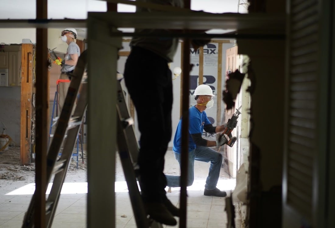 Wide shot of three people working on repairs inside of a building