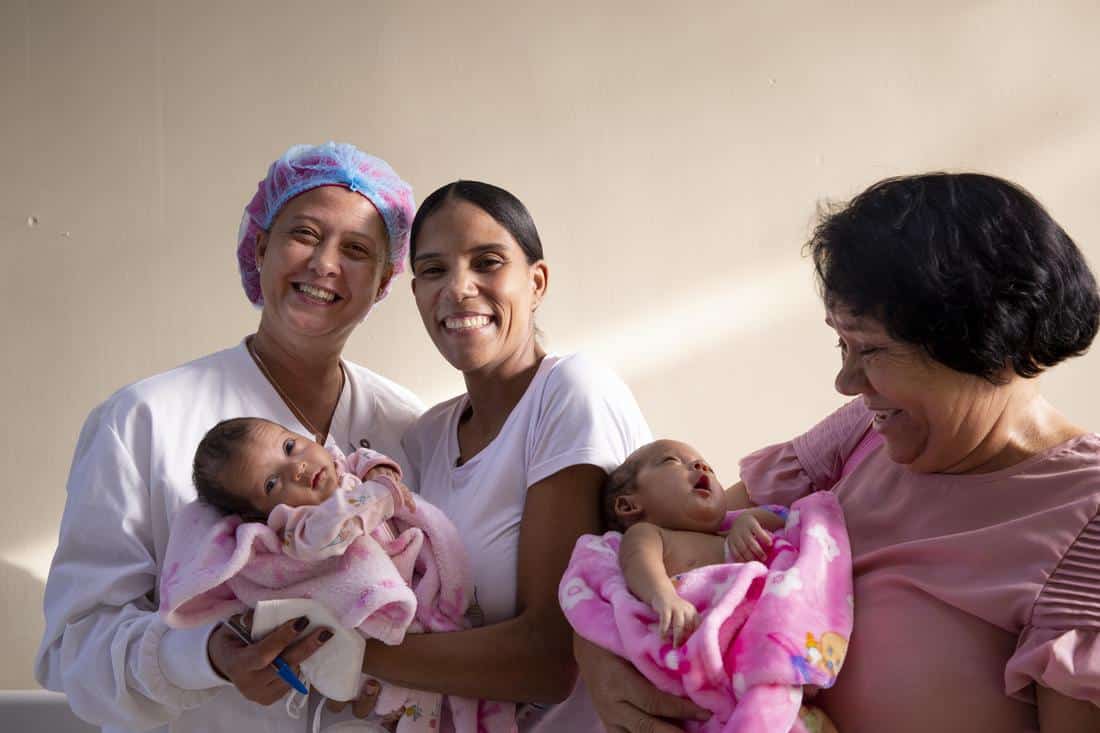 a mother with two woman holding two newborn babies and smiling