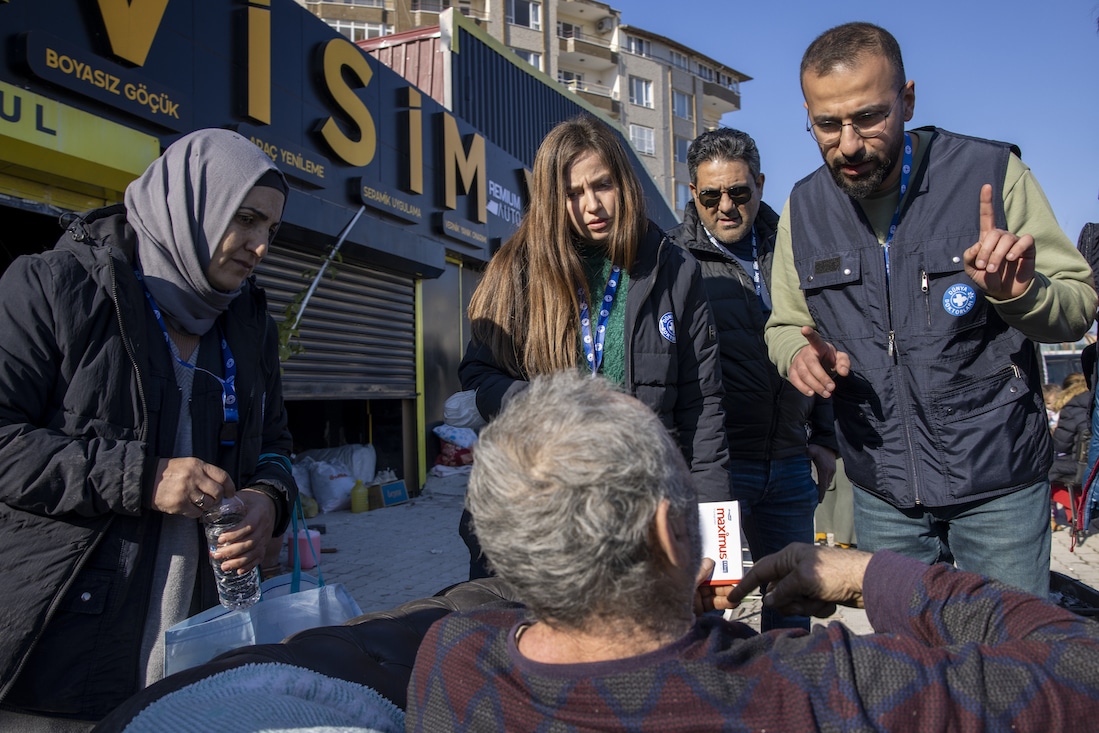 Multiple people checking in on a survivor, facing them, in the middle of a street in Turkiye.