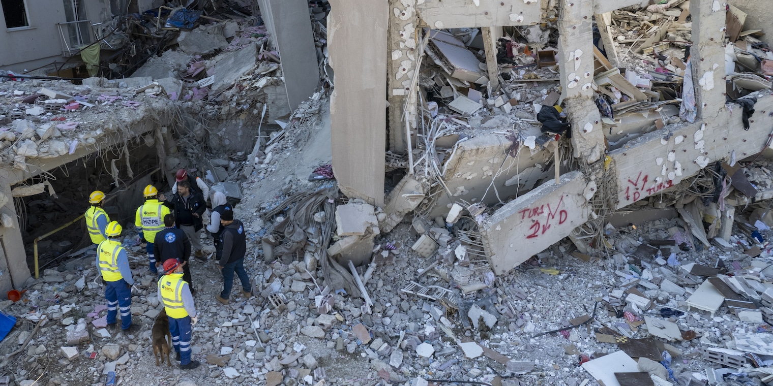 drone (eagle-eye) shot of crew searching within the rubble.