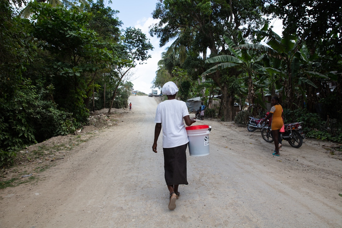 a woman carrying a water bucket away from the camera in Haiti