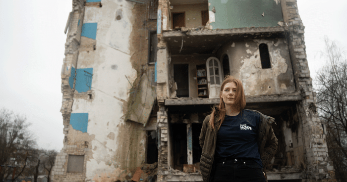 woman stands in front of destroyed building in Ukraine
