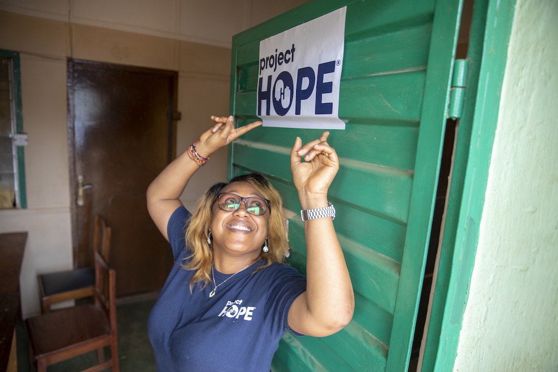 woman leans against door and points to sign reading "Project HOPE" above her