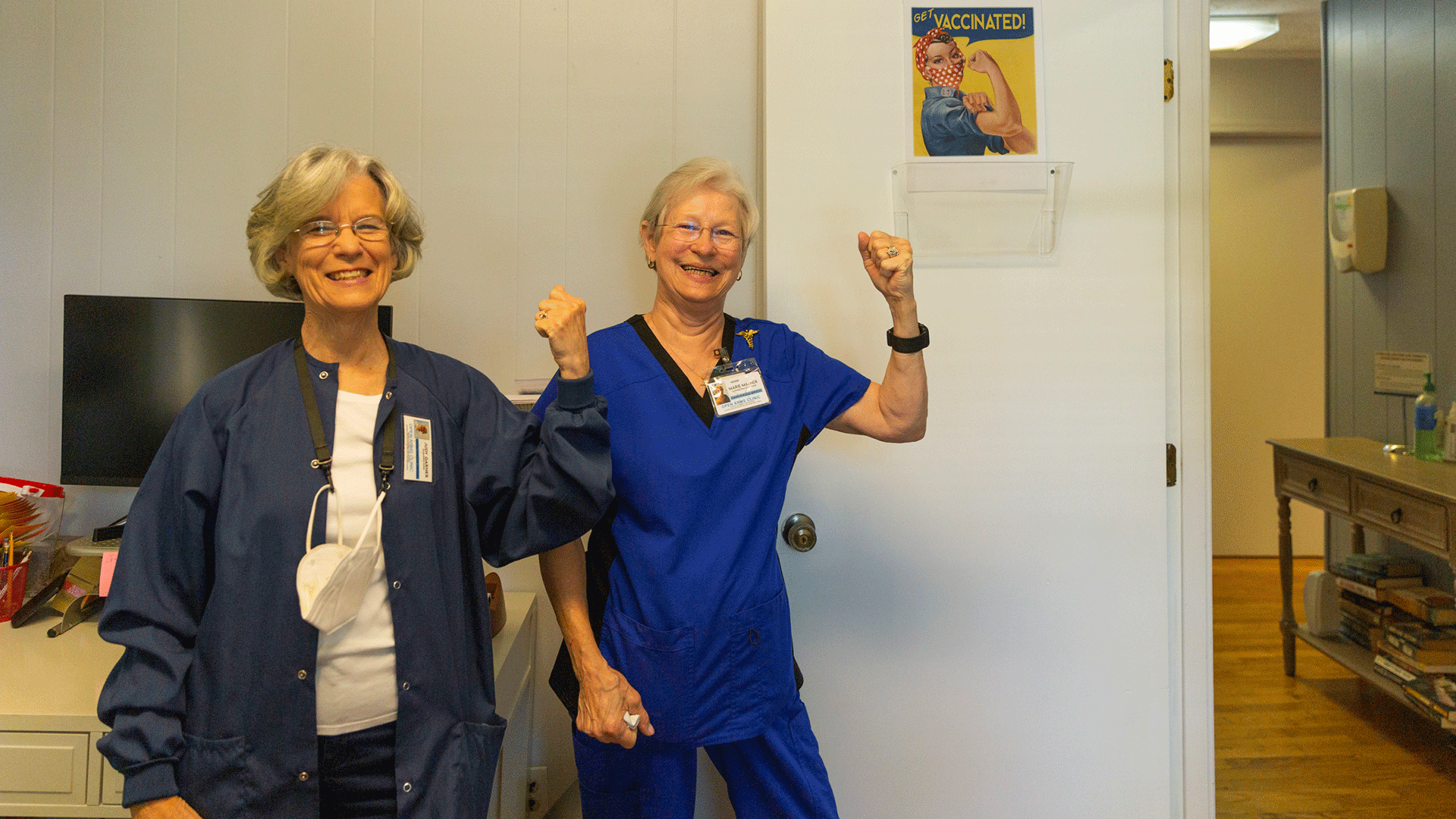 two medical staff posing with a Rosie the Riveter poster to get vaccinated