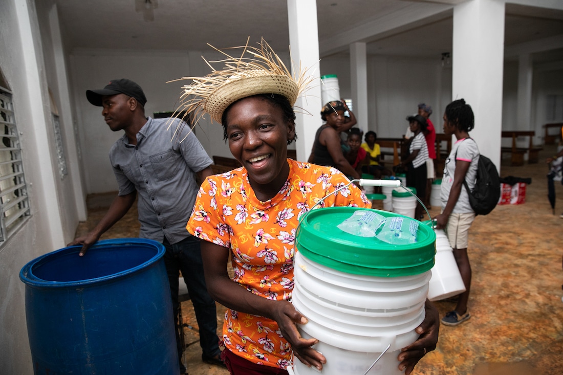 a smiling woman in a straw hat holding a hygiene kit. 