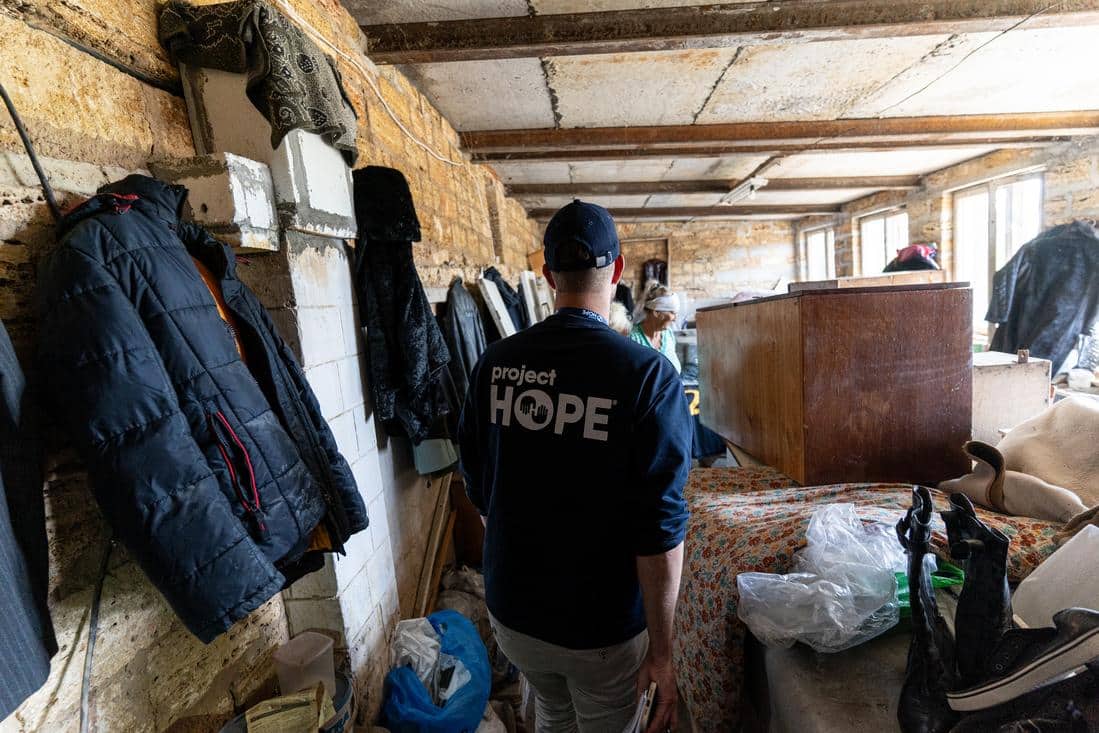 back of man wearing a Project HOPE shirt looking at a damaged house