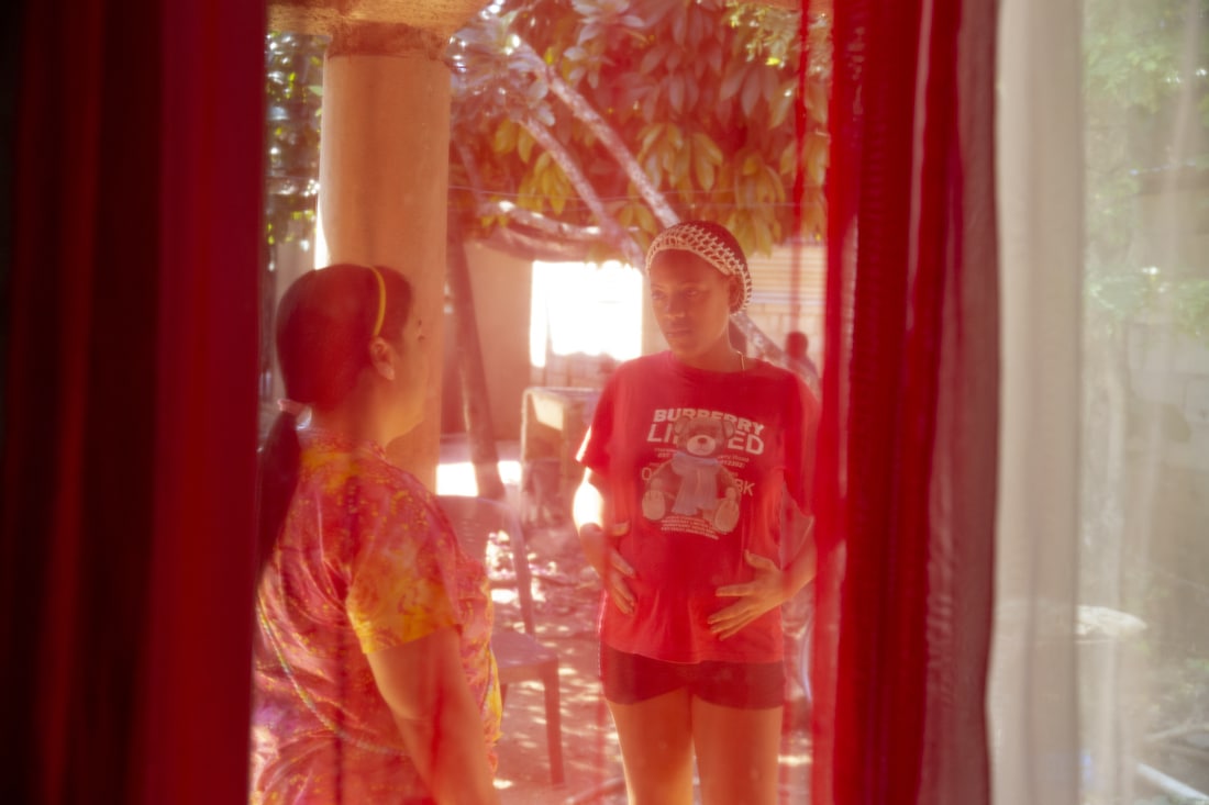 Through a red curtain giving a reddish tint, two women are standing outside talking. 