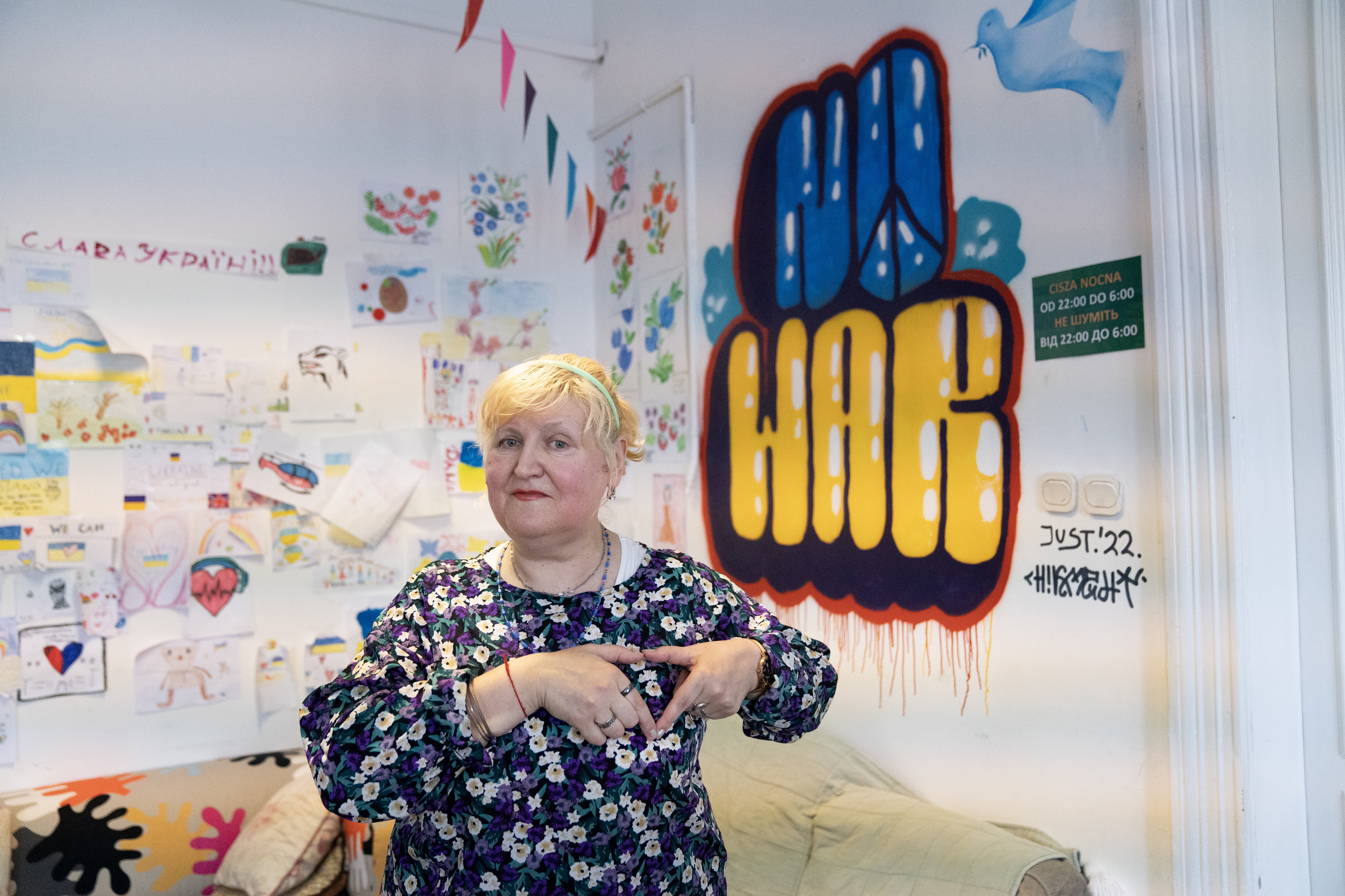 woman makes a heart with her hands in front of a Ukrainian mural that says "No War"