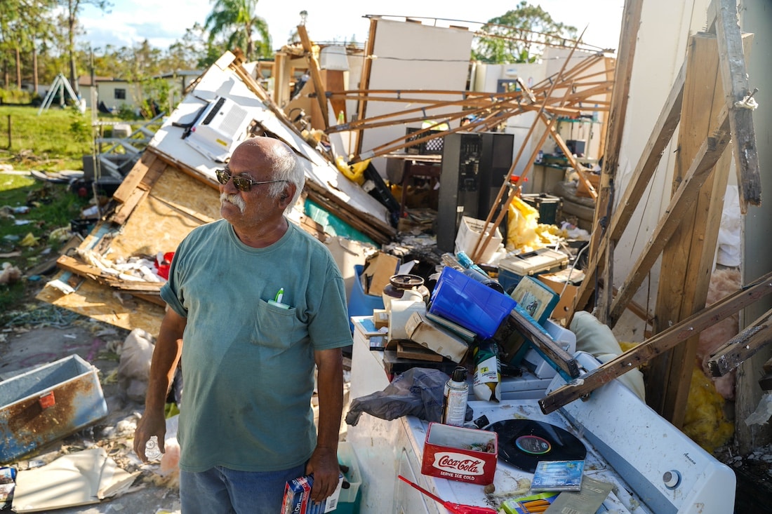man stands in front of destroyed home from hurricane