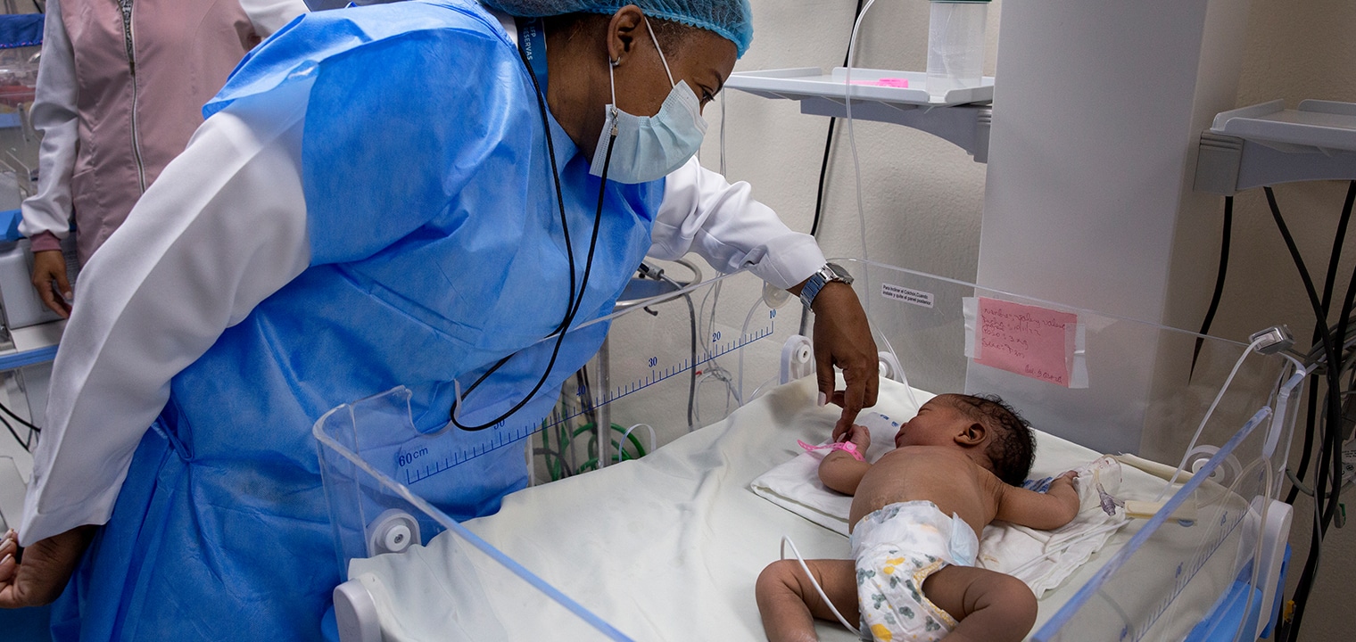 nurse holds onto baby's hand in NICU
