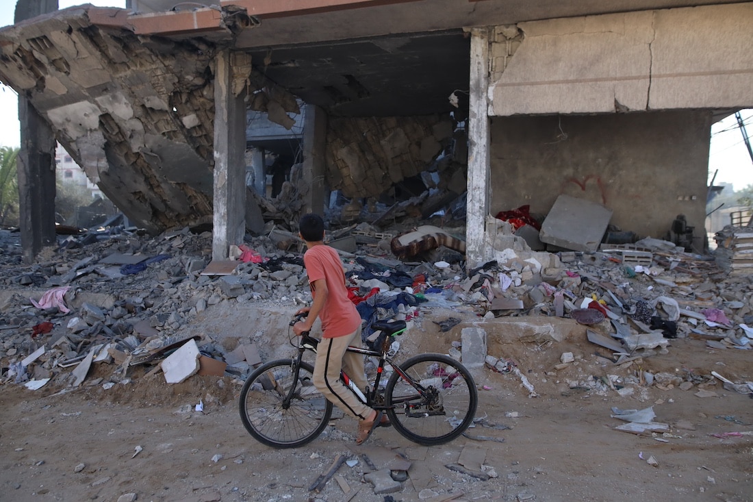 child on bike passes by destruction of building in Gaza