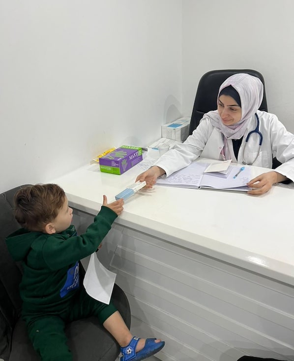 health worker woman handing medical kit to young boy inside an office in Gaza