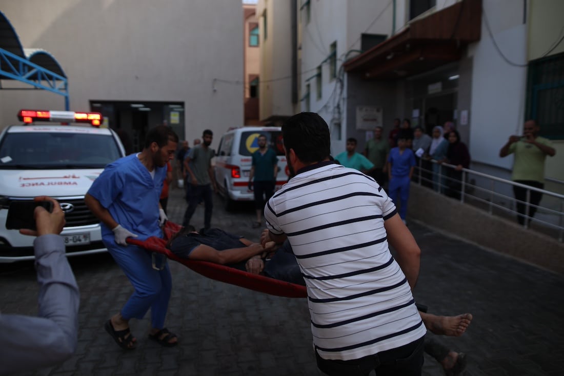 two men carrying a patient on a gurney after an attack in Gaza