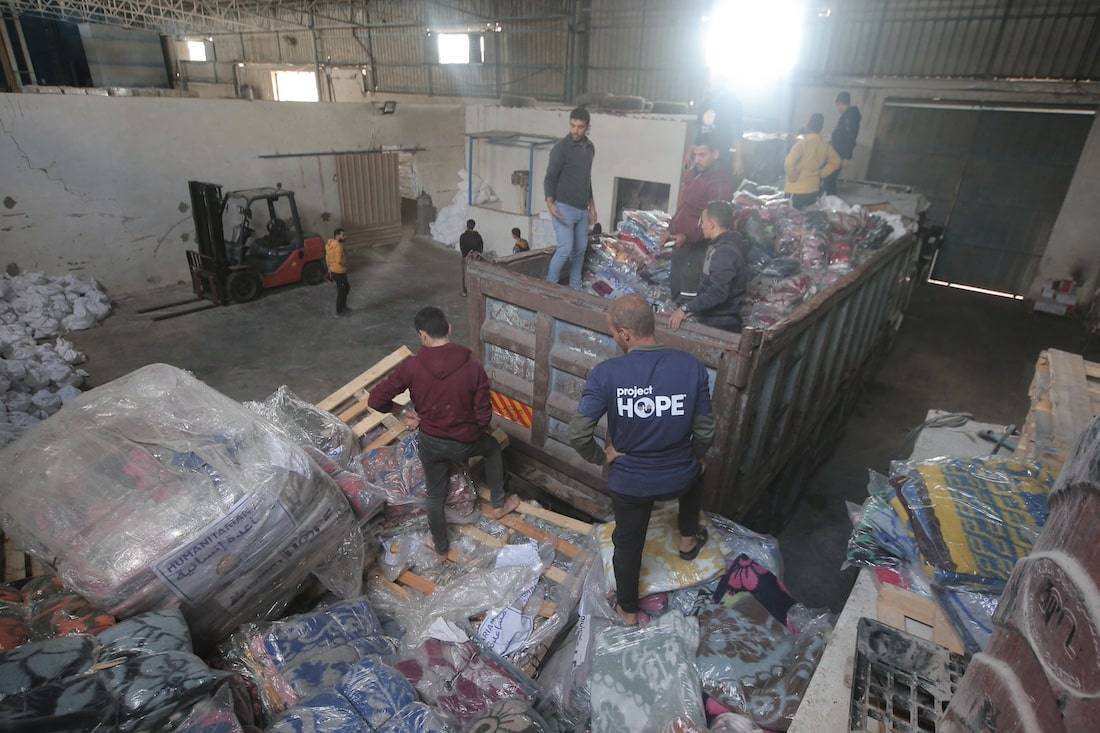 wide angle, eagle-eye shot of a group of people delivering mattresses inside of a warehouse in Gaza