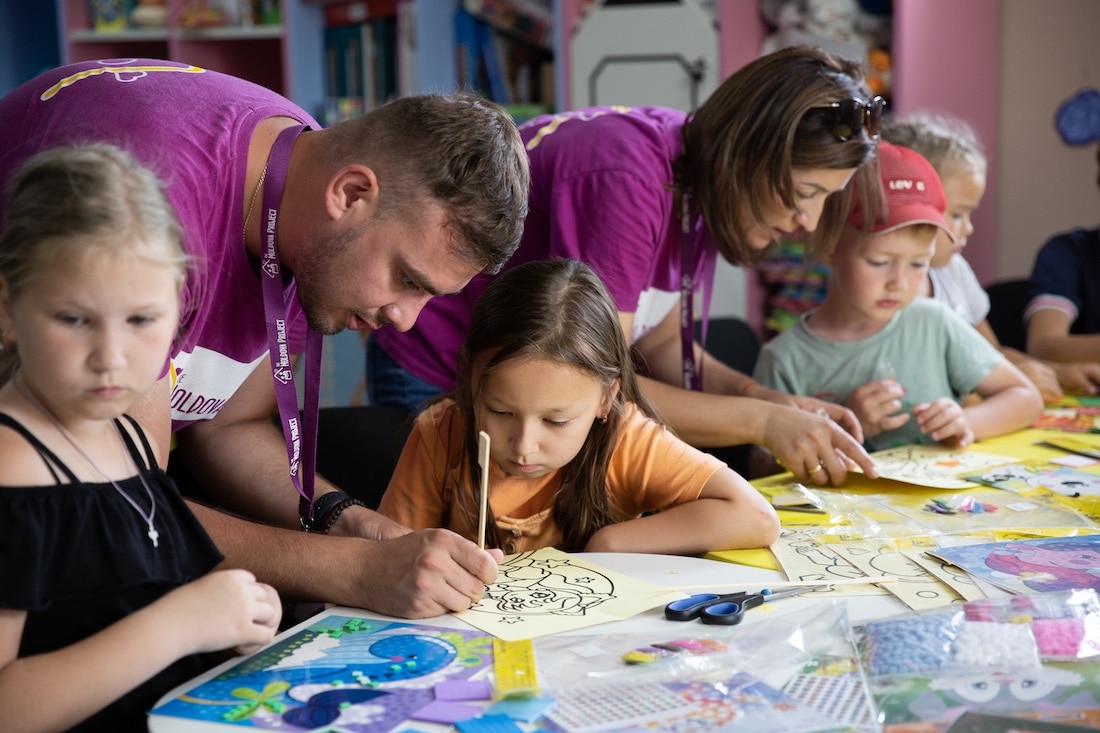 man and woman in purple shirts showing children how to color
