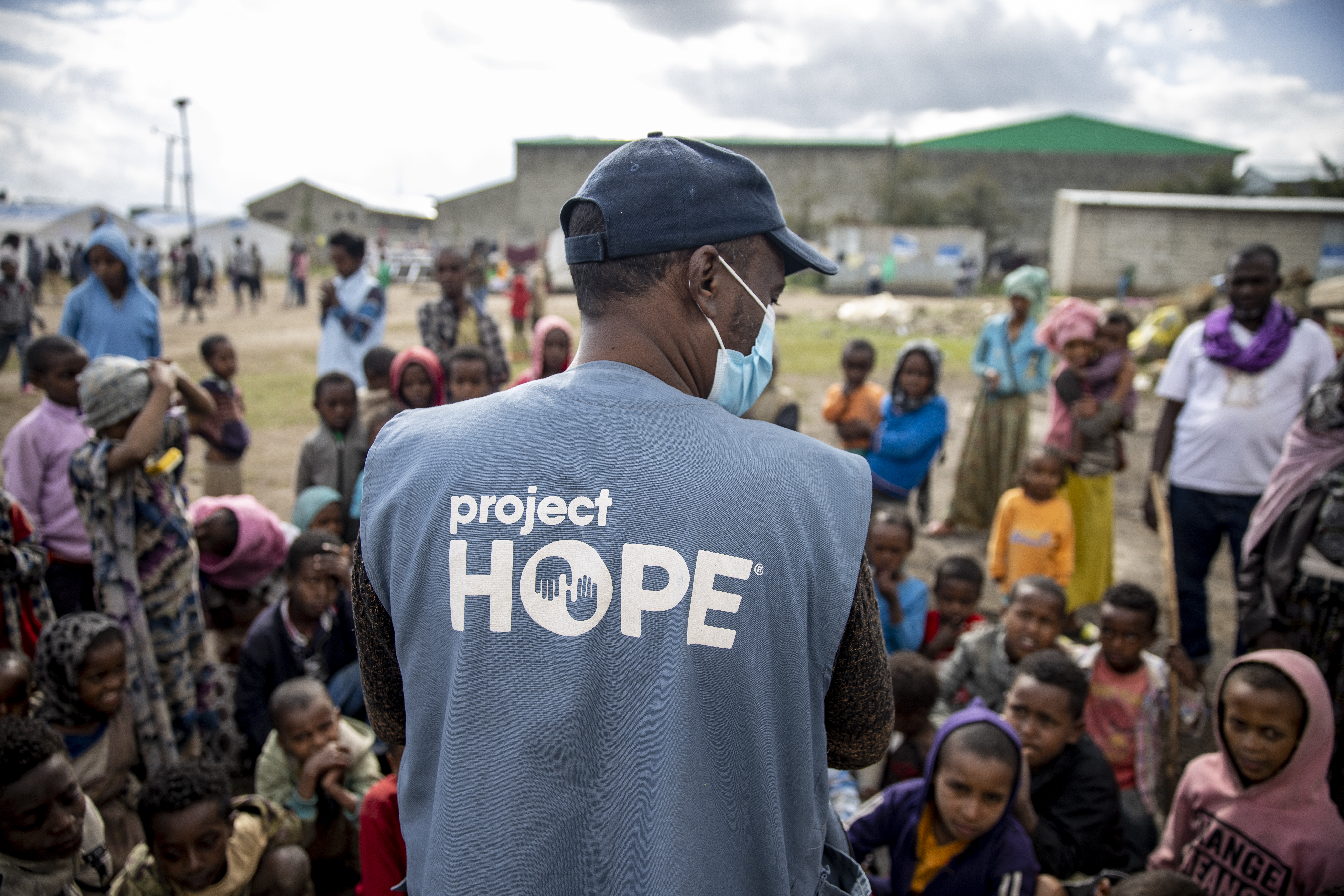 back of man wearing Project HOPE vest as he looks over group of children