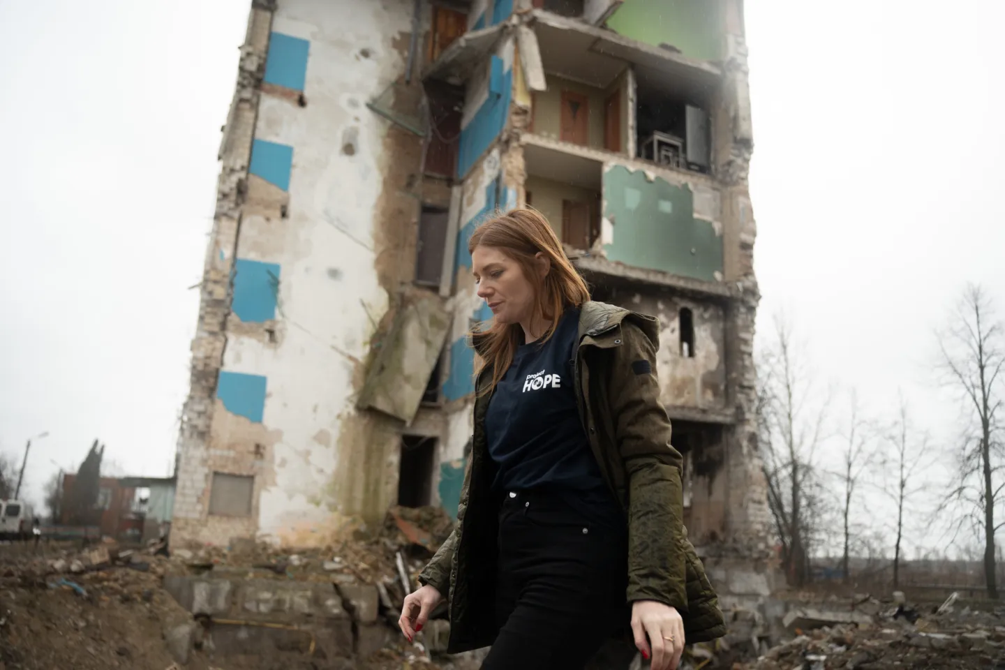 woman stands in front of destroyed building in Ukraine