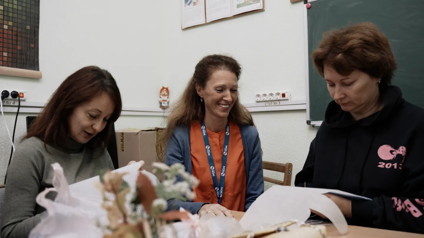 three women sitting at a table doing needlepoint