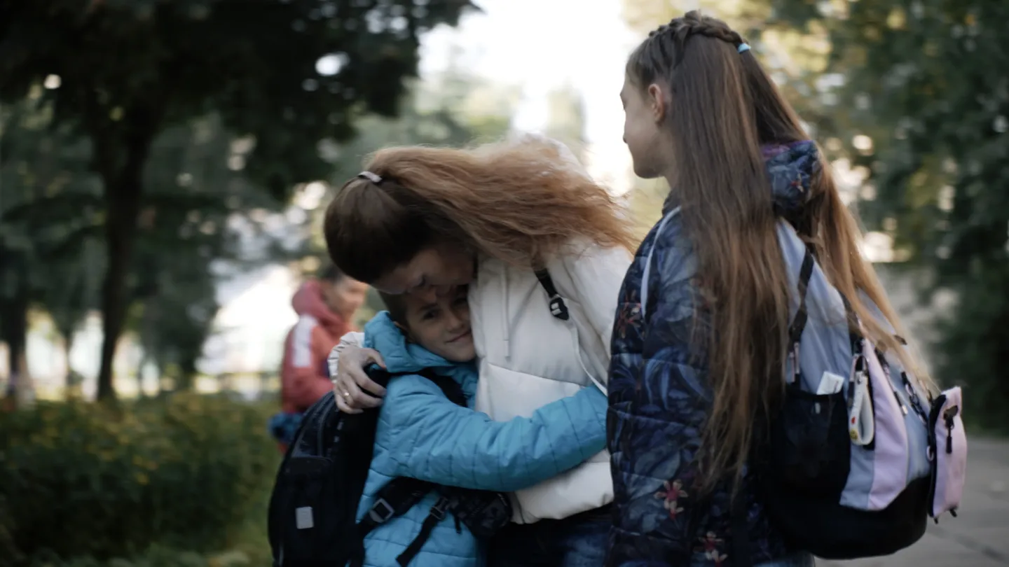 mother hugs young son next to daughter in park
