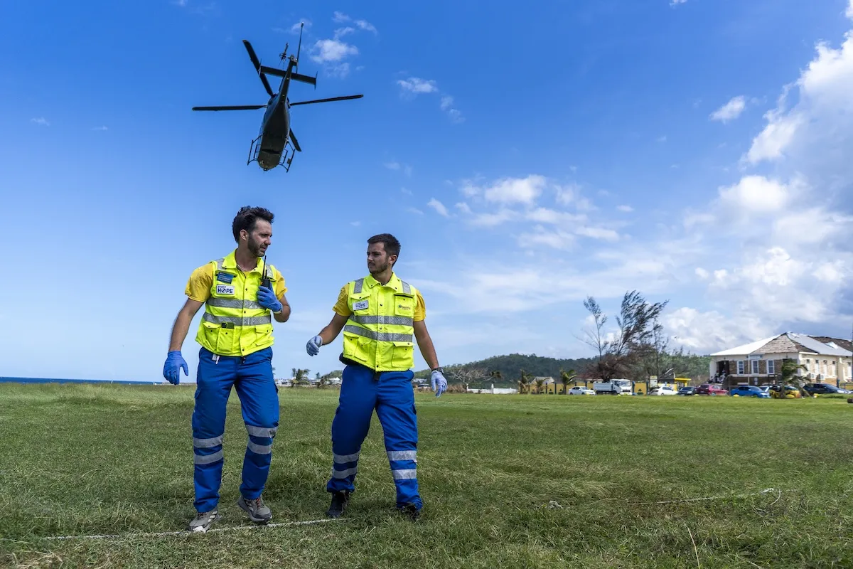 a helicopter takes off while two emergency response staff are on the ground