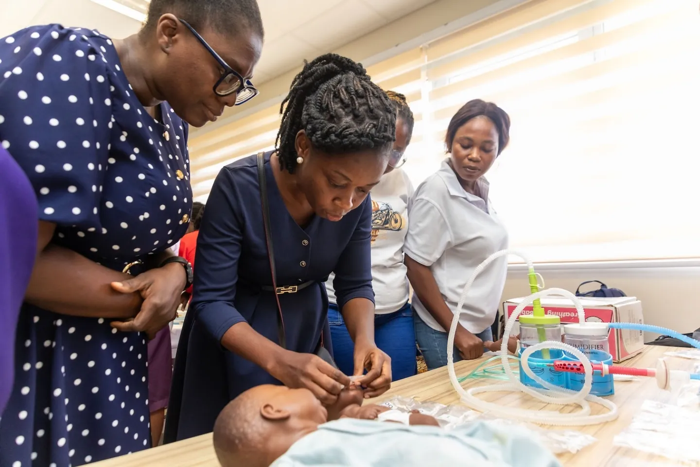 women learn how to apply a cpap machine to a doll to prepare for using on newborns