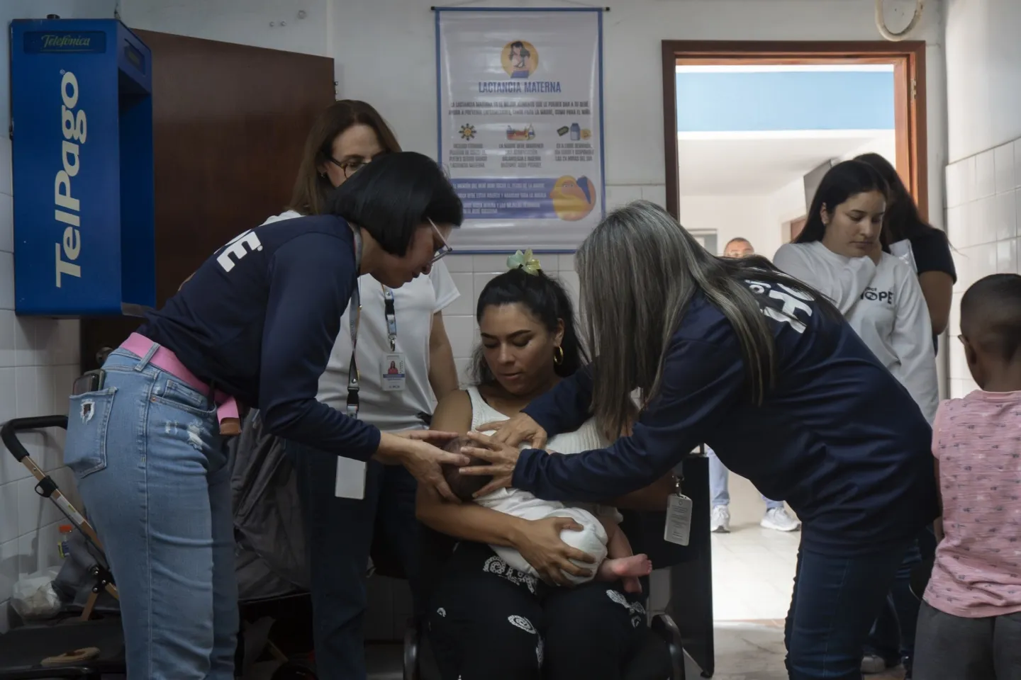 new mother is taught how to latch newborn to her breast by two Project HOPE staff members inside clinic in Venezuela