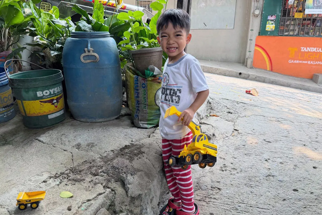 young boy plays with toy truck and smiles at the camera