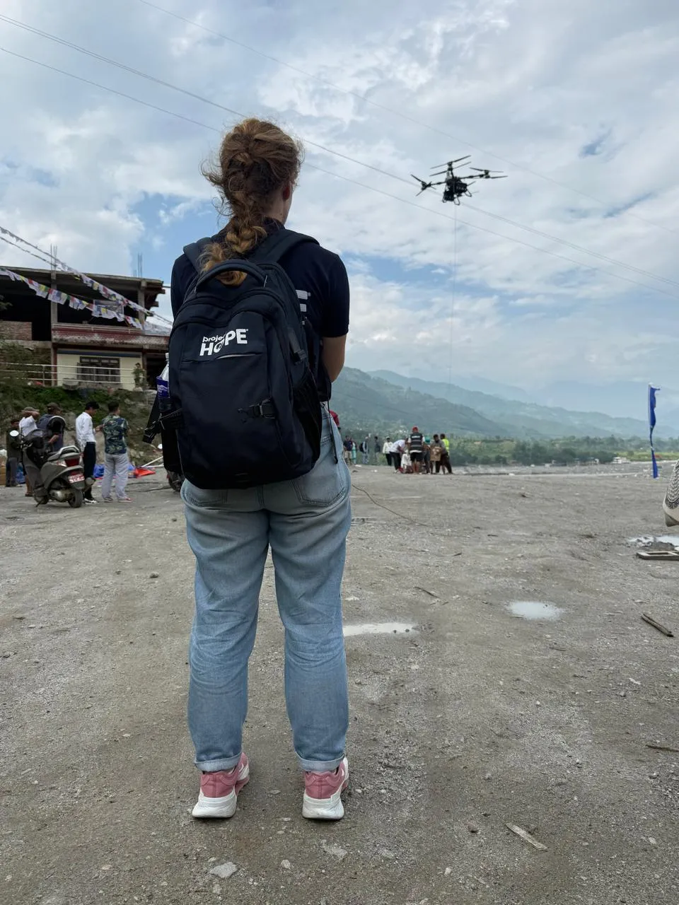 back of woman as she controls a drone over Nepal grounds after a flood.